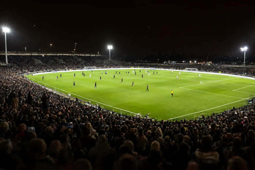 Empty football stadium pitch at dusk with floodlights switched on above the stands